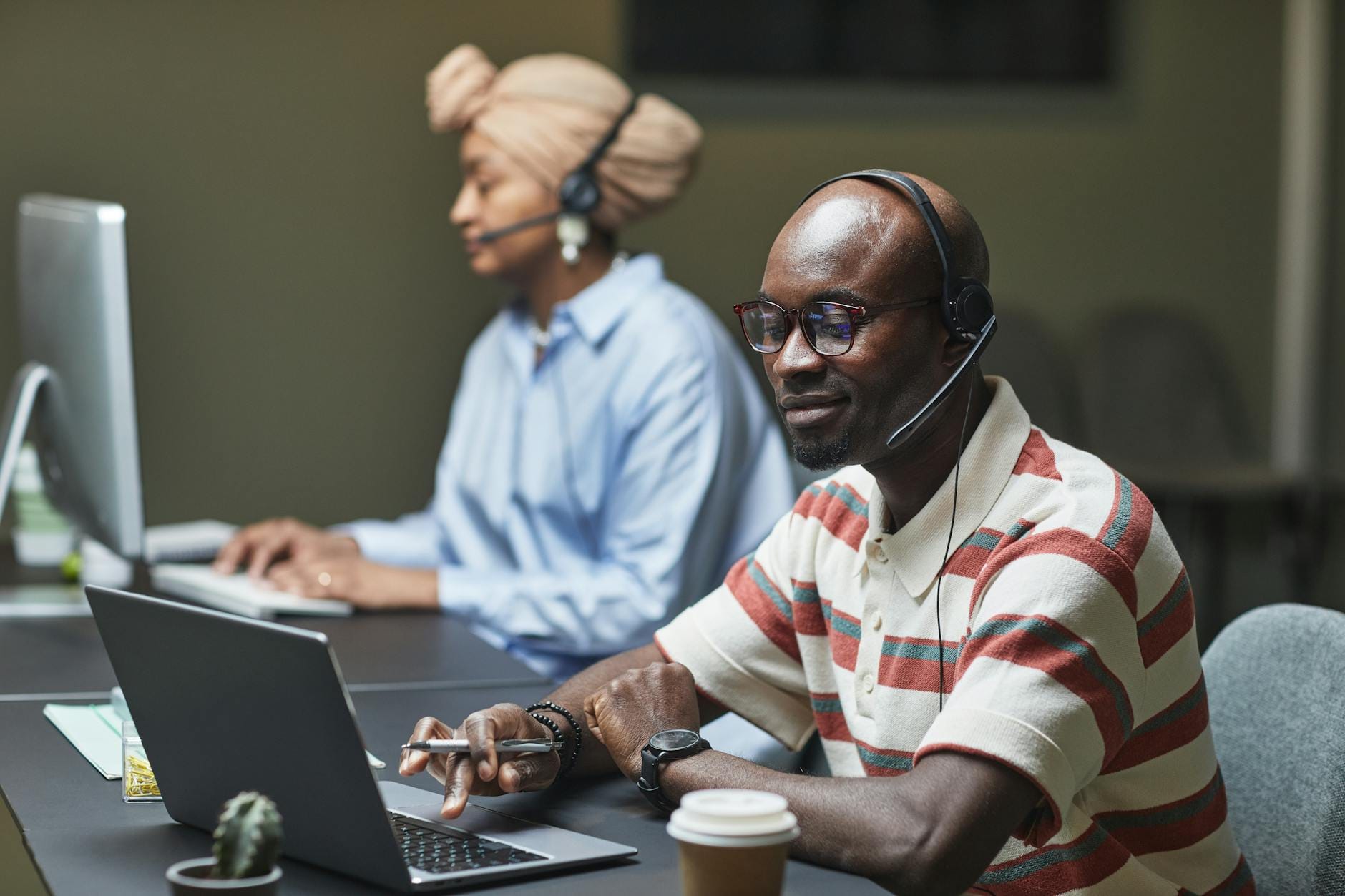 Two customer support employees working on computers with headsets in a modern office.