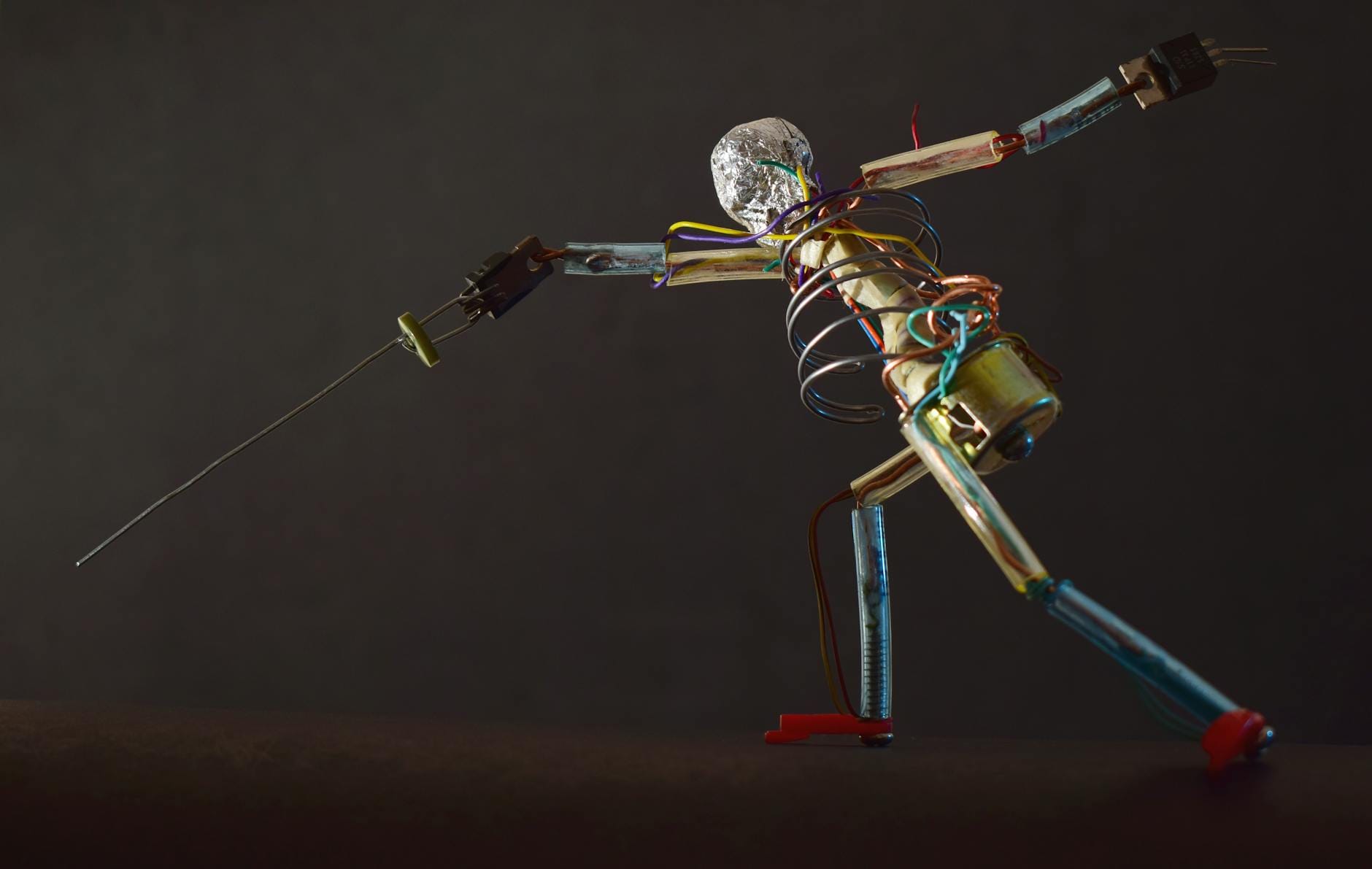 Metallic robot sculpture in a dynamic fencing pose with wires and parts, shot in São Paulo.