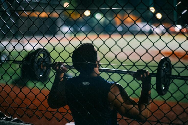 A man lifting weights behind a chain fence at night, showcasing strength and fitness.