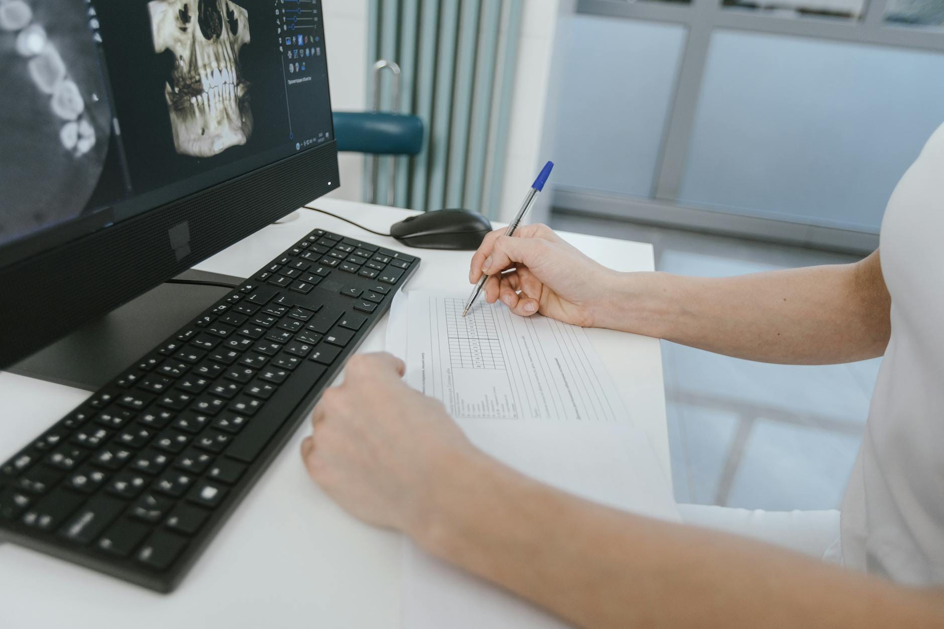 Close-up of a healthcare worker analyzing x-ray results and taking notes on a computer desk.