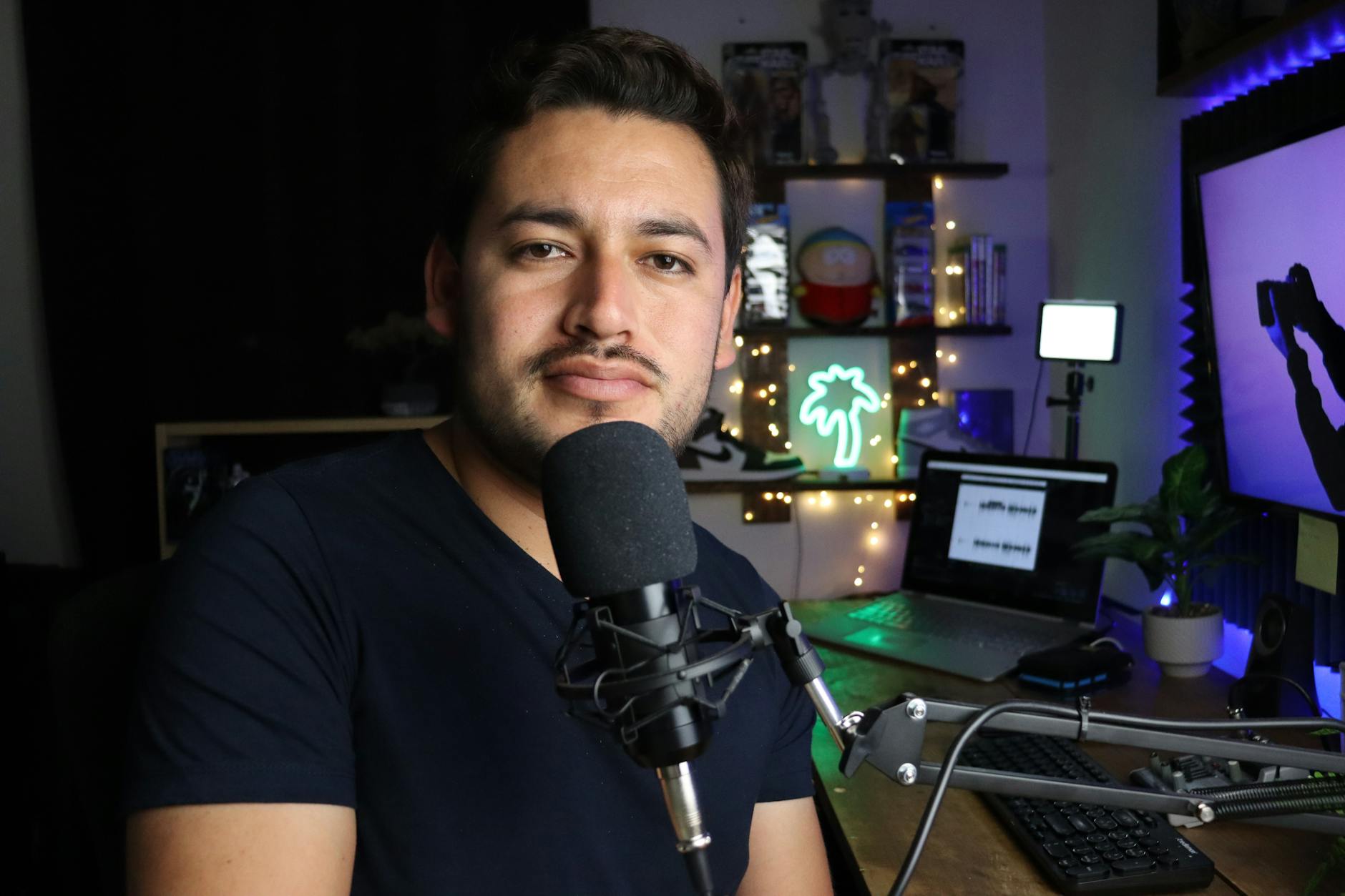 A podcaster in a home studio with neon lighting and tech equipment.