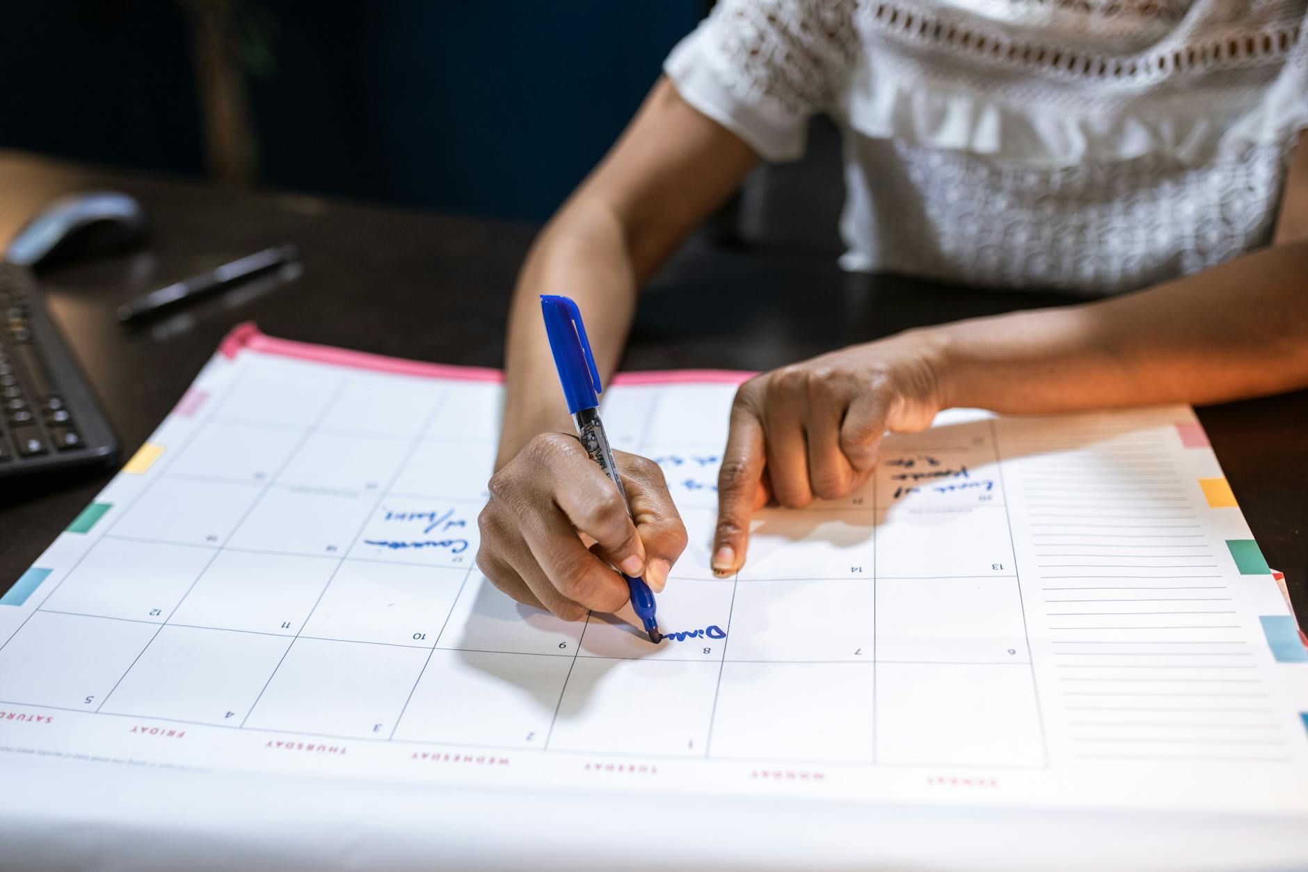 A woman marks important dates on her desk calendar, planning upcoming events.