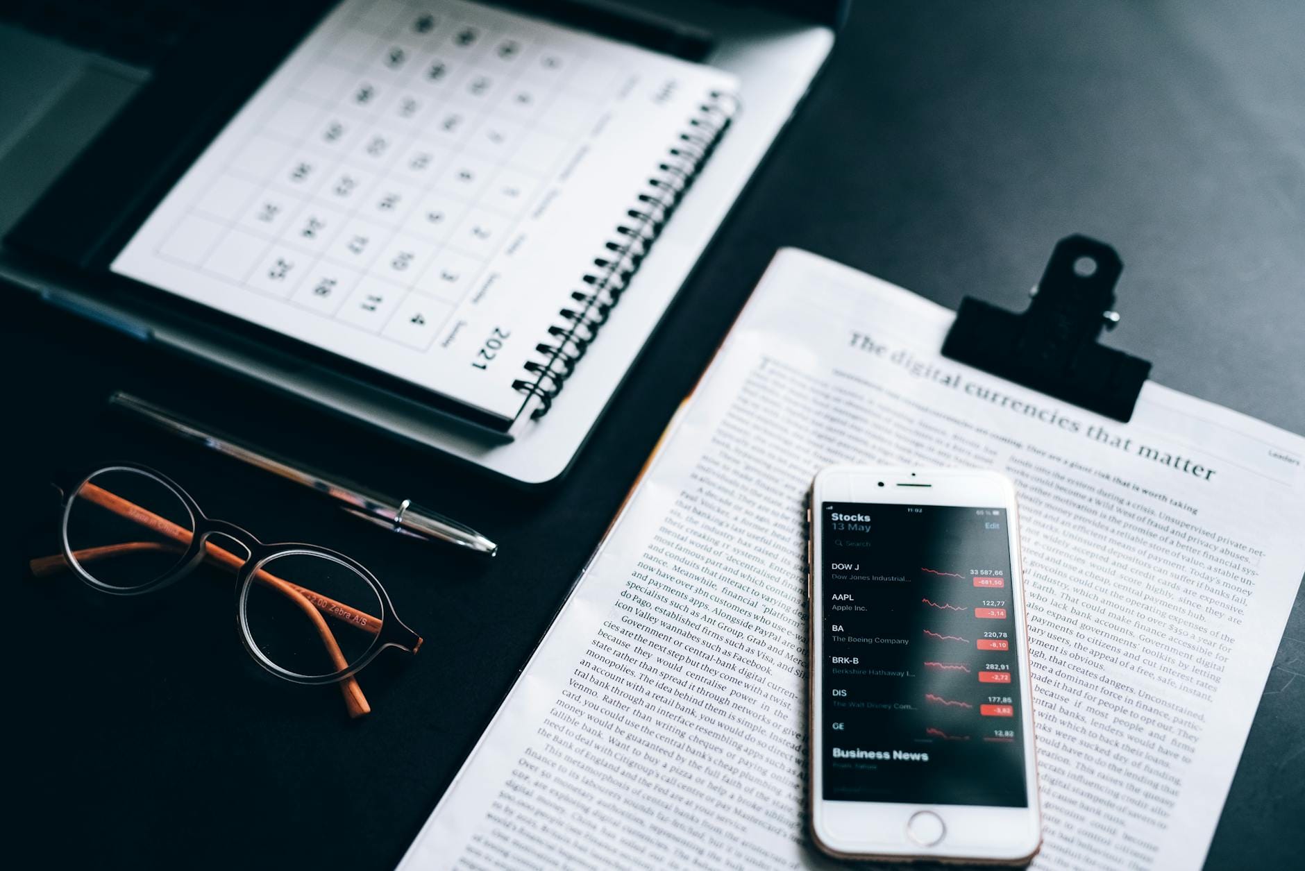 High angle shot of a desk setup with smartphone displaying stock market analytics, clipboard, pen, and glasses.