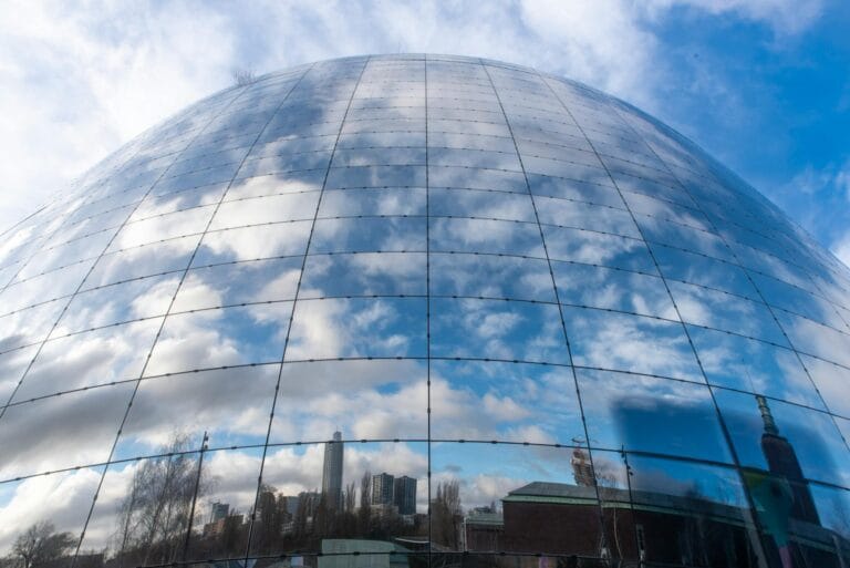 A large reflective dome captures a vibrant city skyline with clouds overhead, creating a stunning mirror effect.