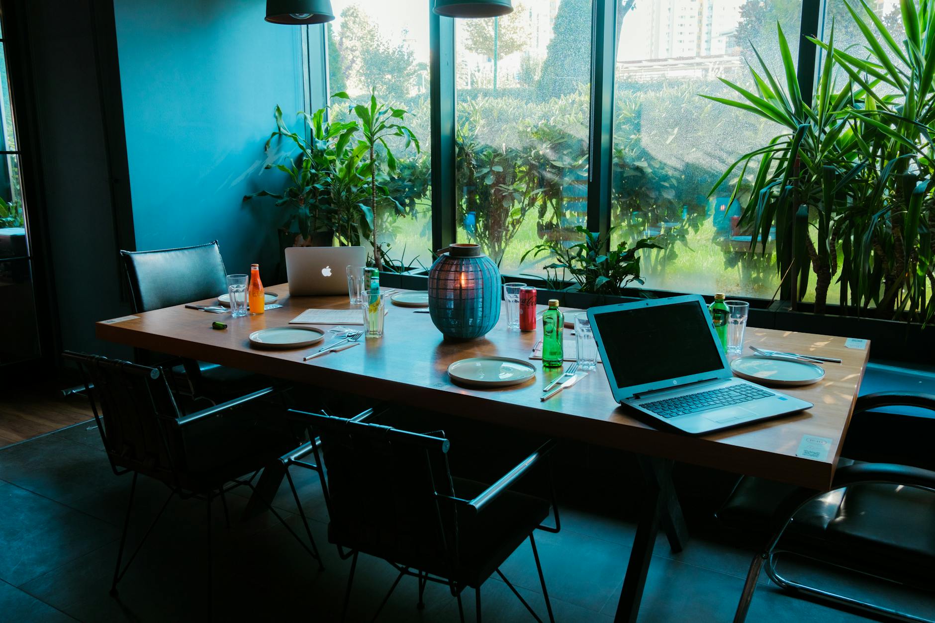Modern office meeting room with laptops, drinks, and lush greenery.
