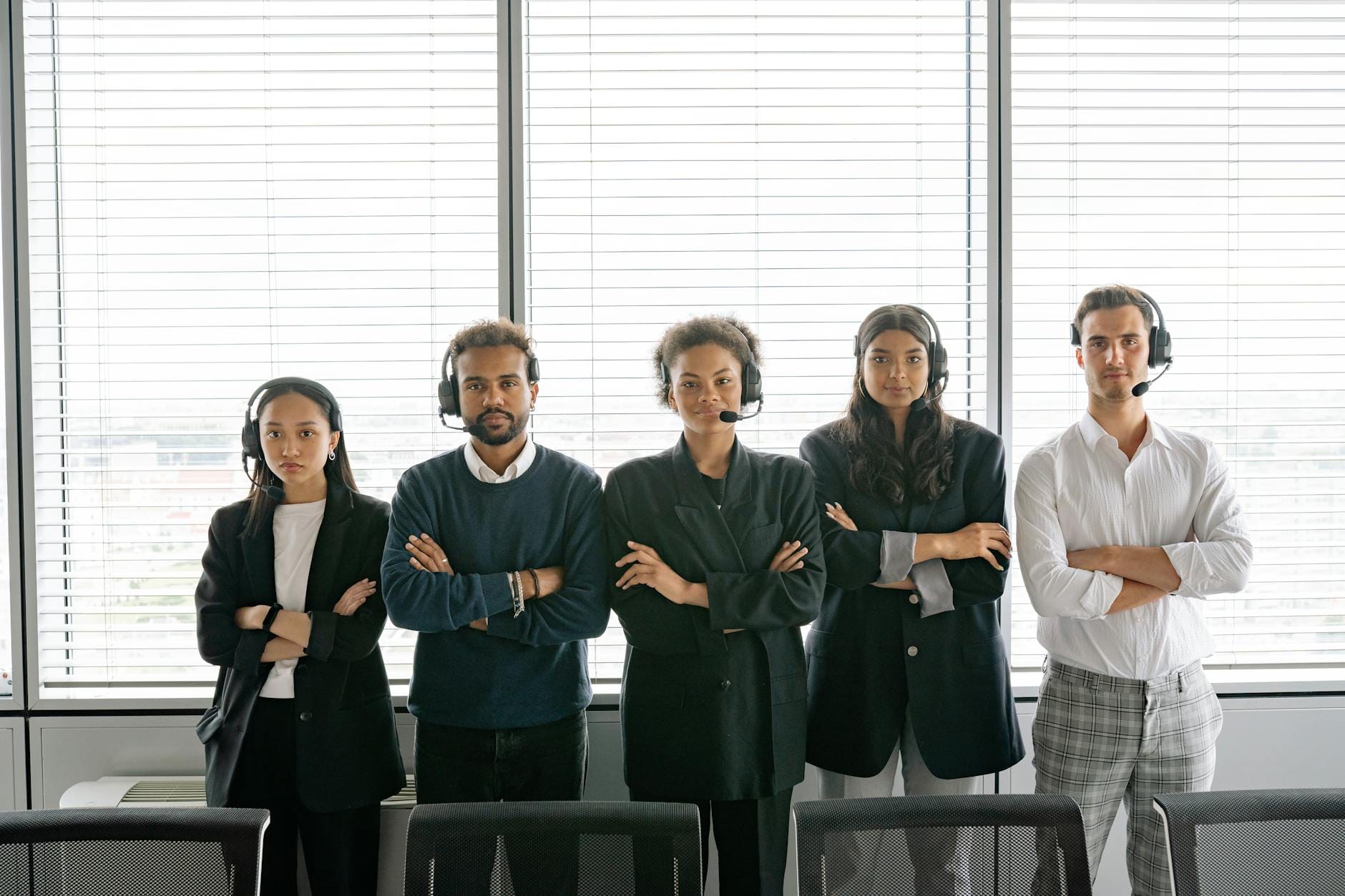 A diverse group of call center agents standing with arms crossed, wearing headsets in an office.