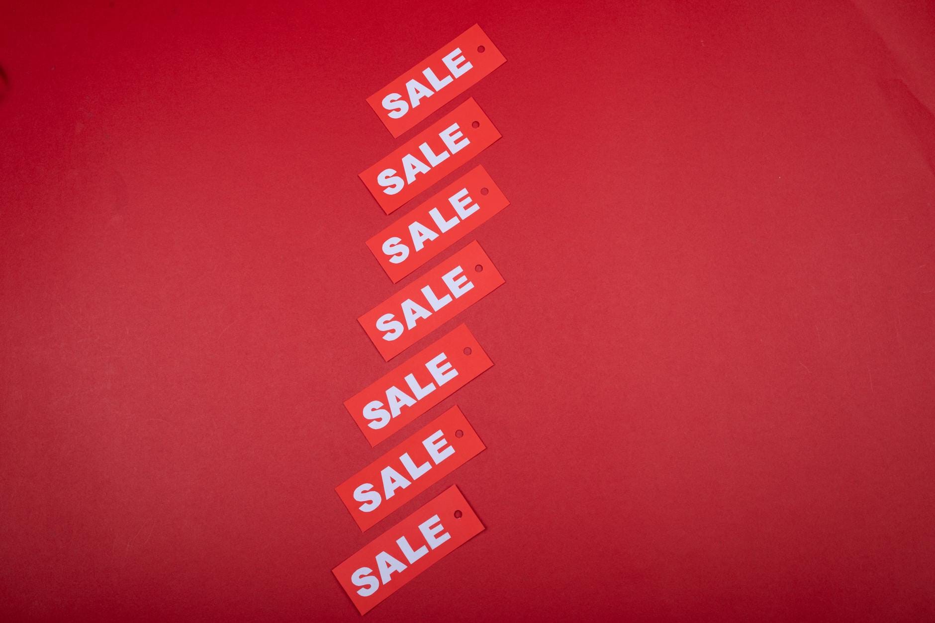 Top view of red sale tags arranged on a vibrant red background for commercial use.