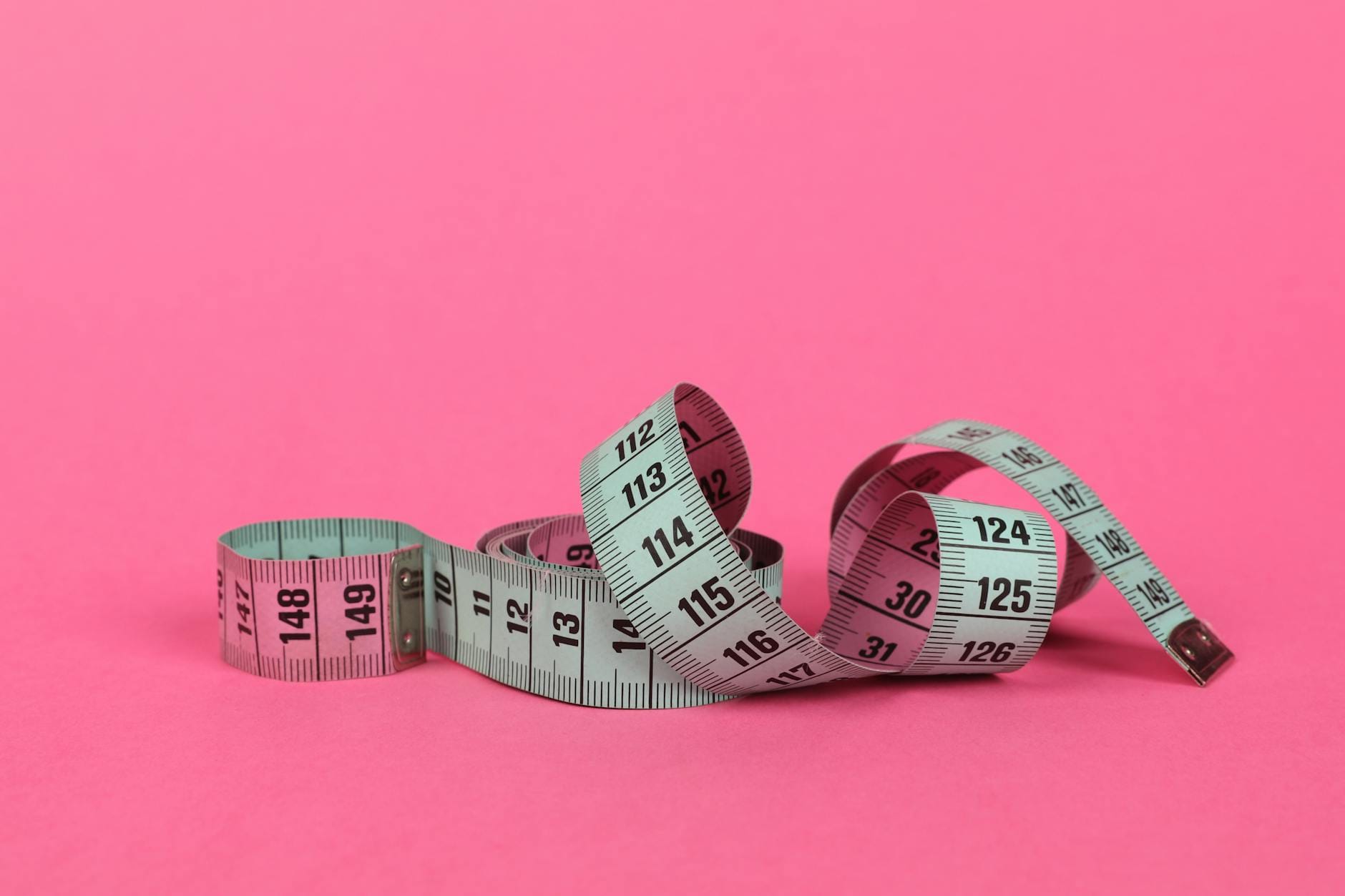 Close-up of a measuring tape on a vibrant pink background for design use.