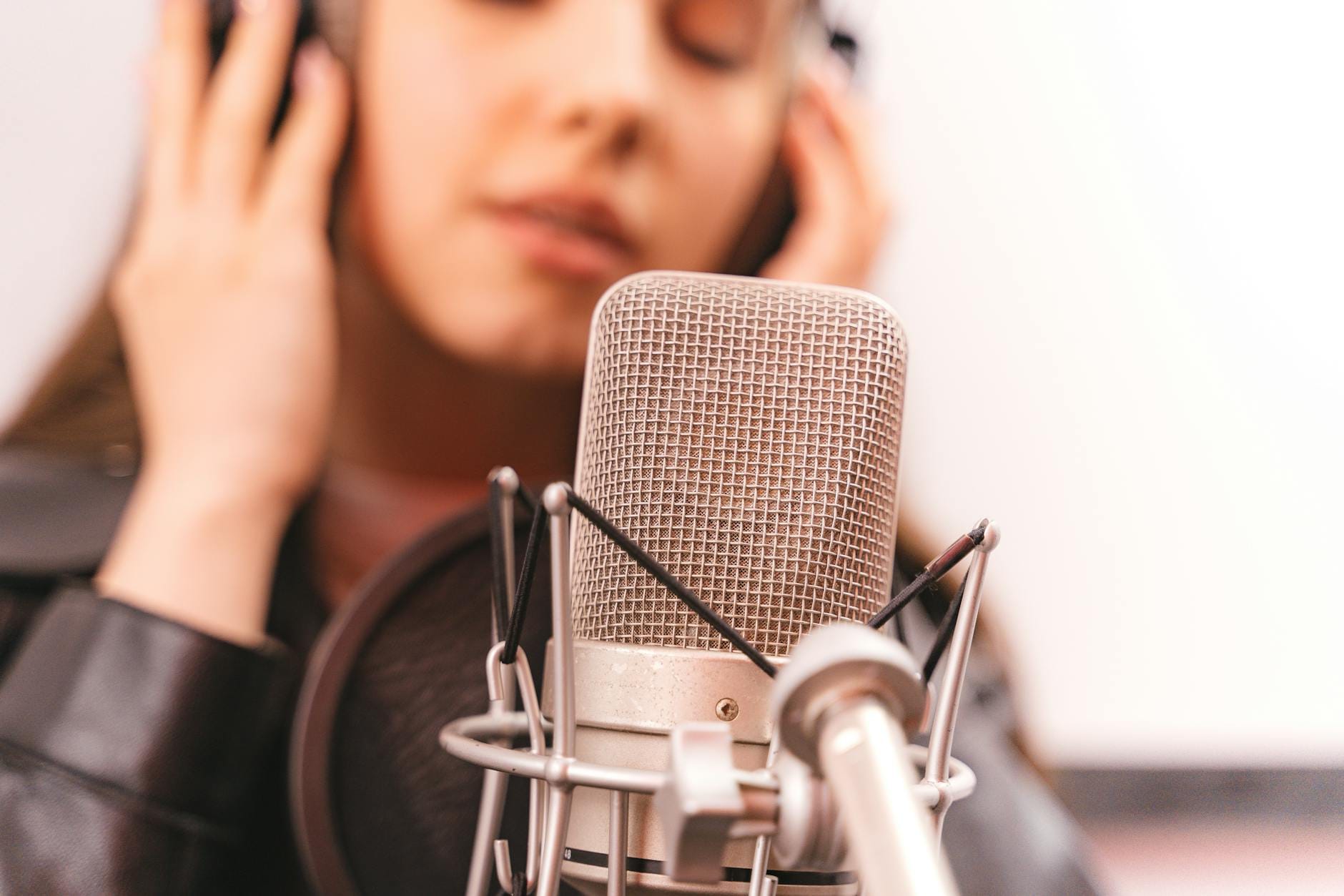 Close-up of a woman singing into a studio microphone, eyes closed, expressing emotion.