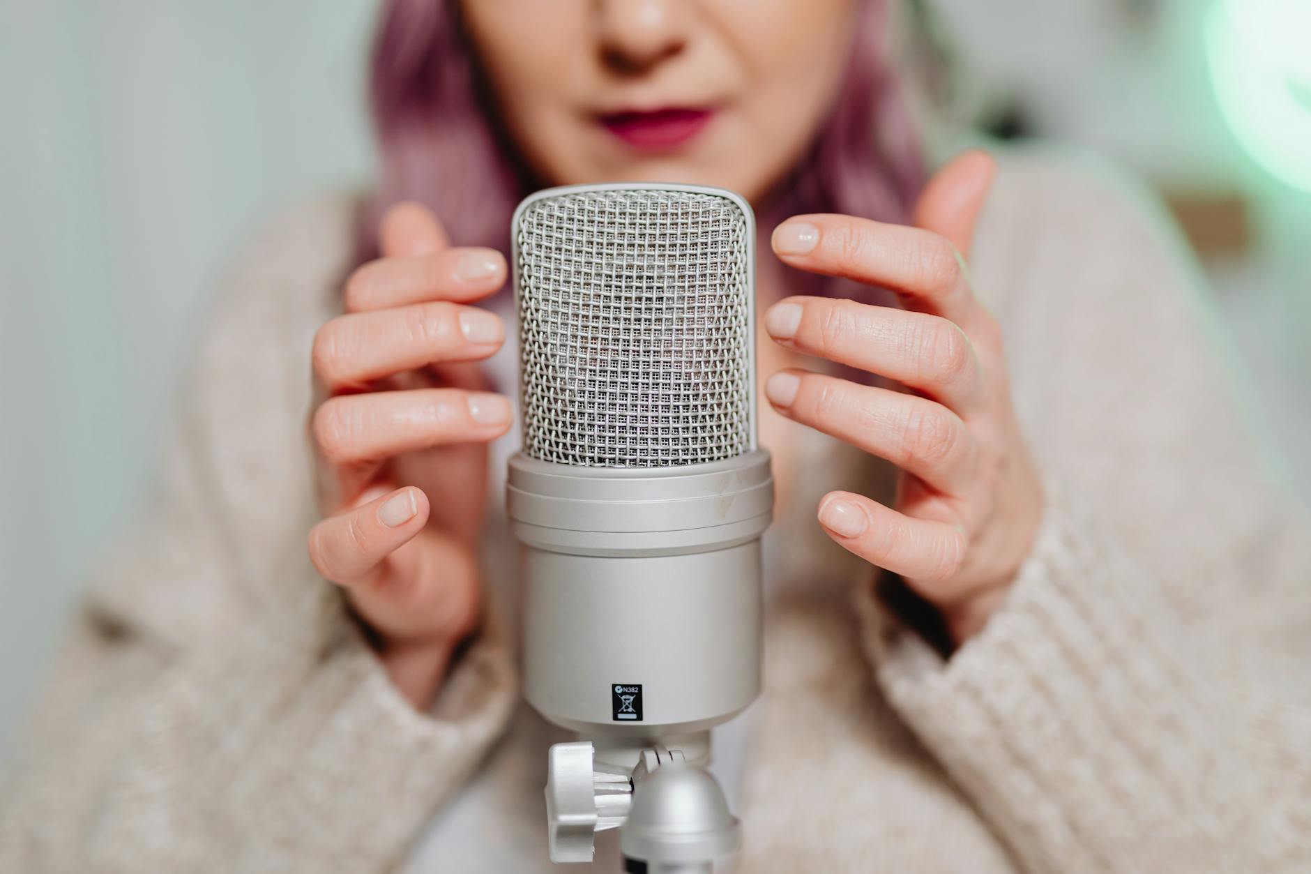 Close-up of a woman recording ASMR audio with a microphone indoors.