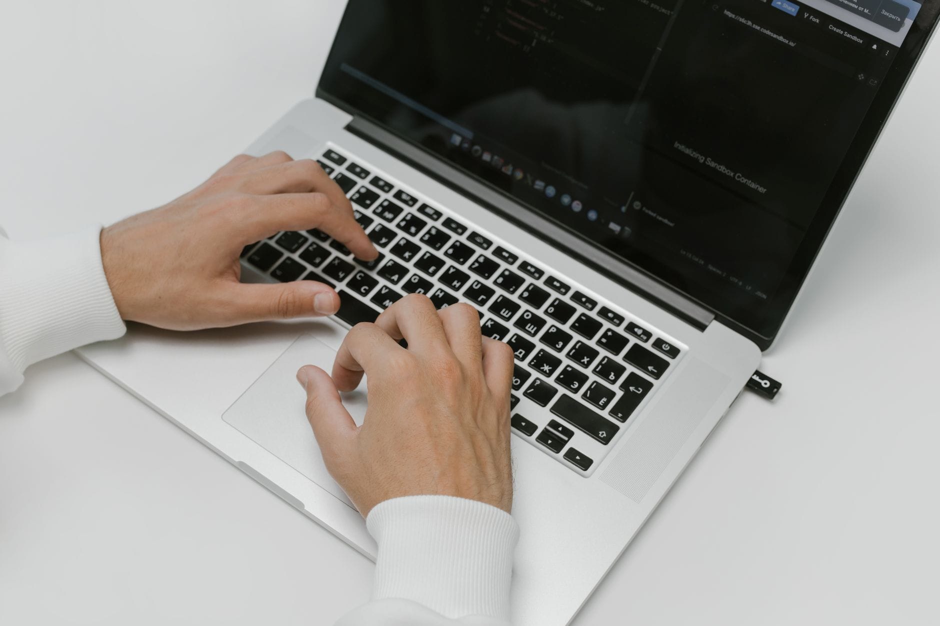 Close-up of hands typing on a laptop with a USB device on a white background. Ideal for tech and cybersecurity themes. —