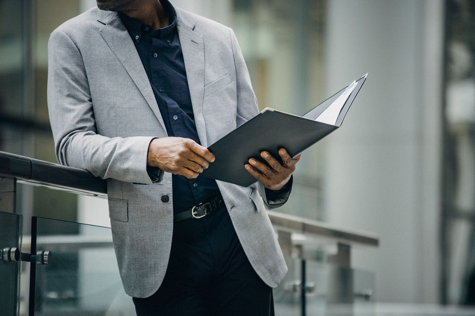 Crop unrecognizable black man in elegant suit reading documents leaning on railing on city street — best ai meeting tool