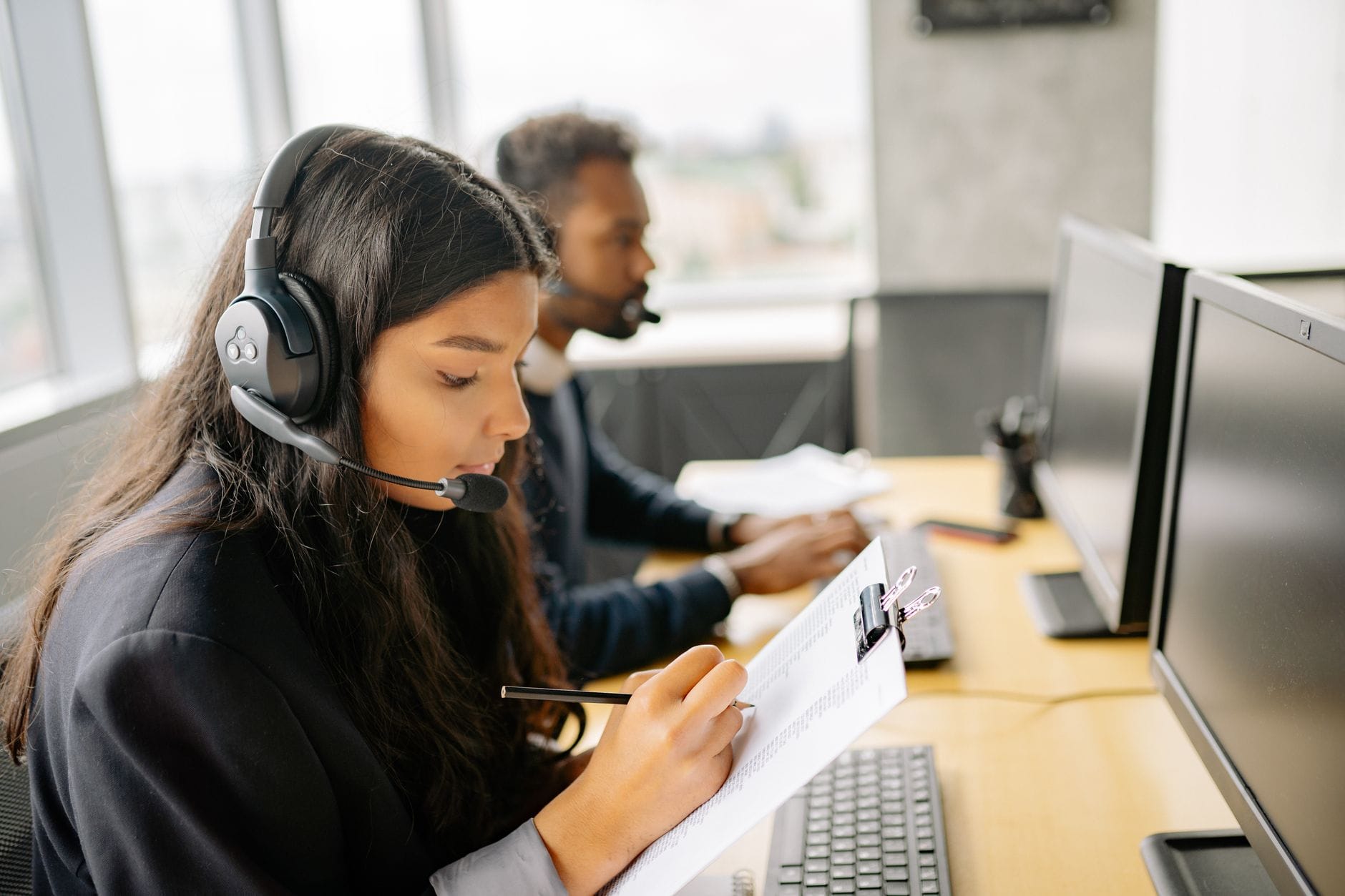 Two call center agents wearing headsets working at desks with computers in a modern office. — best ai meeting tools 2026