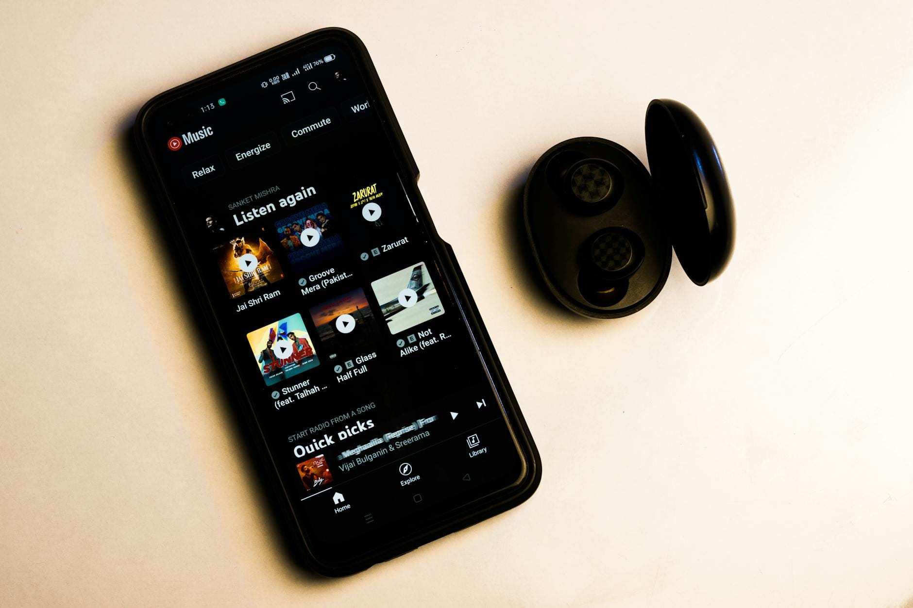 A smartphone displaying a music app interface with wireless earbuds on a plain background. — elevenlabs music app ai mus