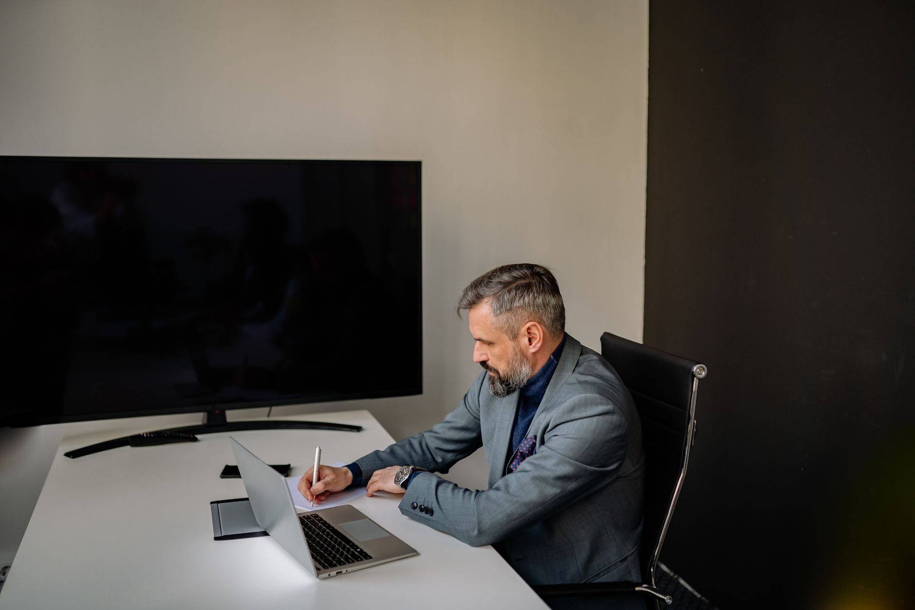 Bearded businessman in formal attire writing notes at a modern office workspace. — gamma app review 2026