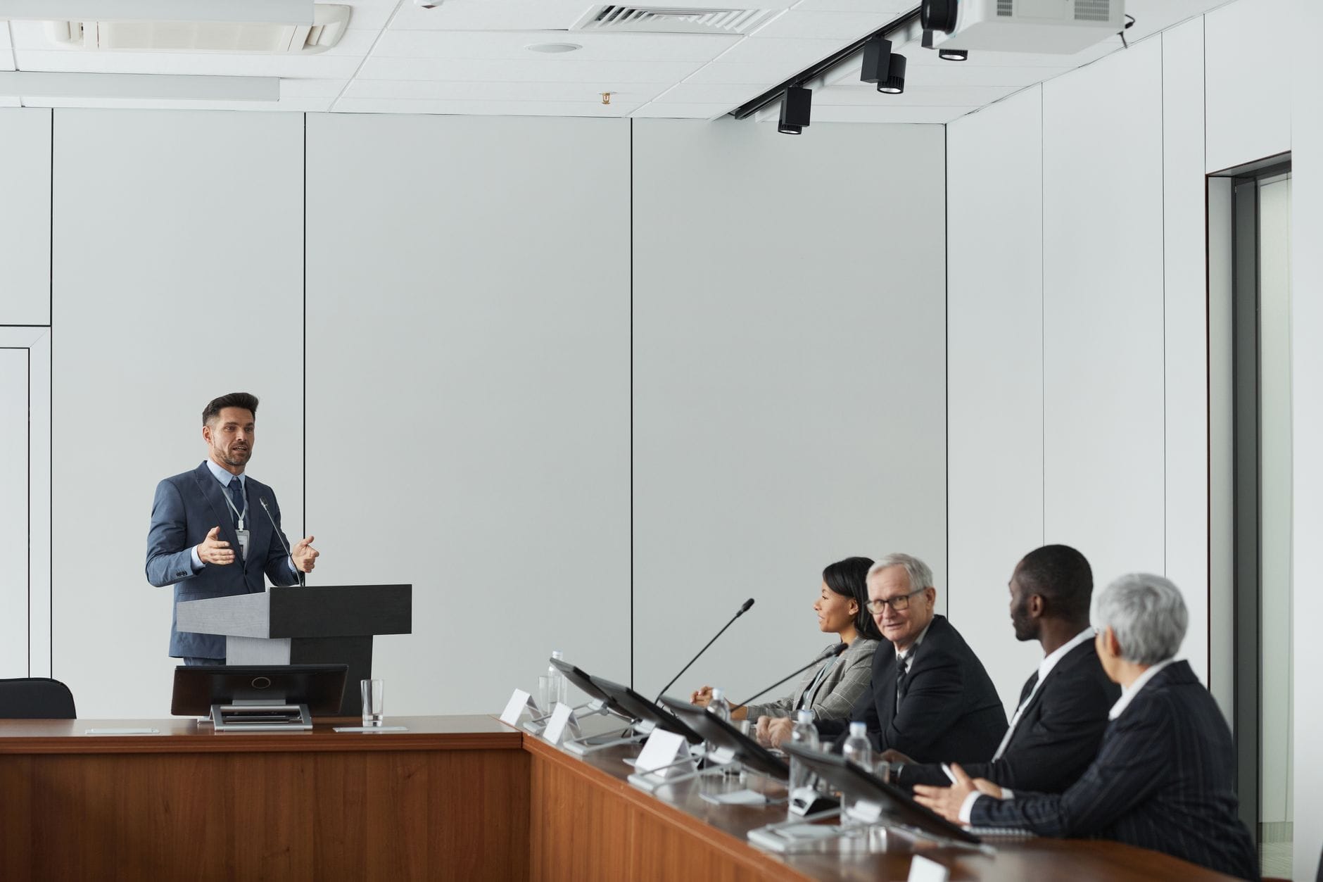 Formal business meeting with a speaker at the podium addressing a diverse panel in a conference room. — claude mania ent