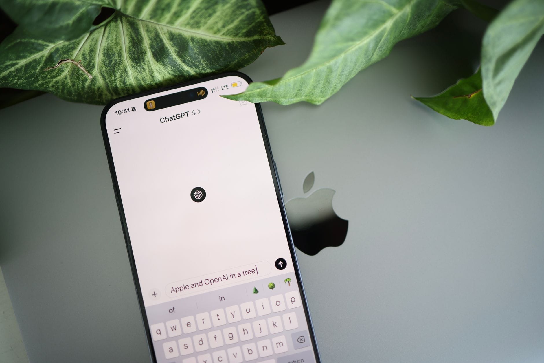 A smartphone shows a ChatGPT interface placed on an Apple laptop in a leafy environment. — manychat review 2026
