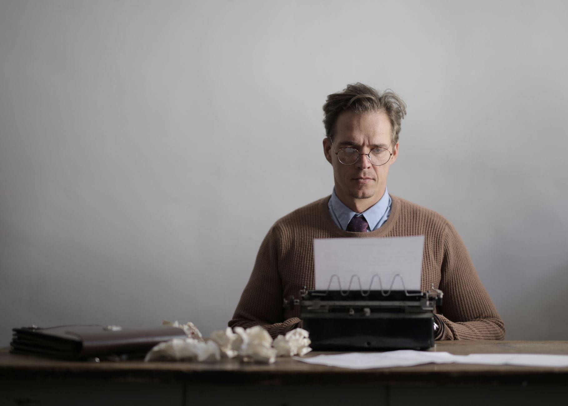 A thoughtful male writer typing on a vintage typewriter, surrounded by crumpled papers. — taplio review 2026