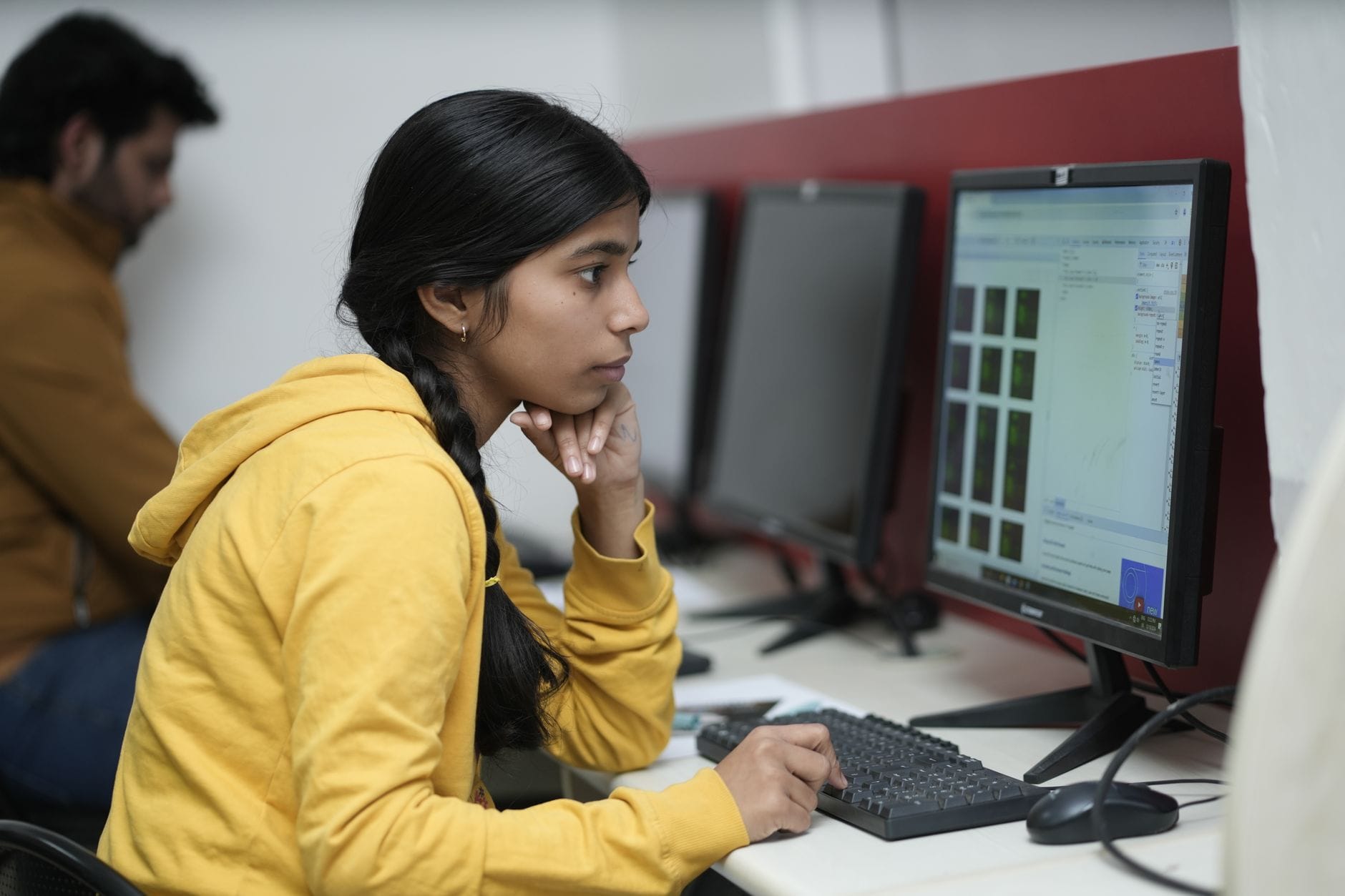 Woman in yellow hoodie focused on computer work, indoor office. — openai cybersecurity model staggered rollout 2026