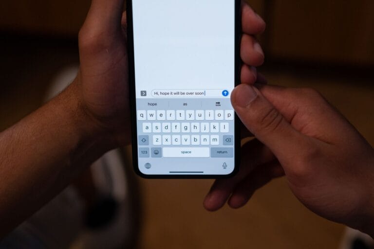 Close-up of hands texting on a smartphone indoors with a hopeful message on screen. — new siri release date iphone 2026