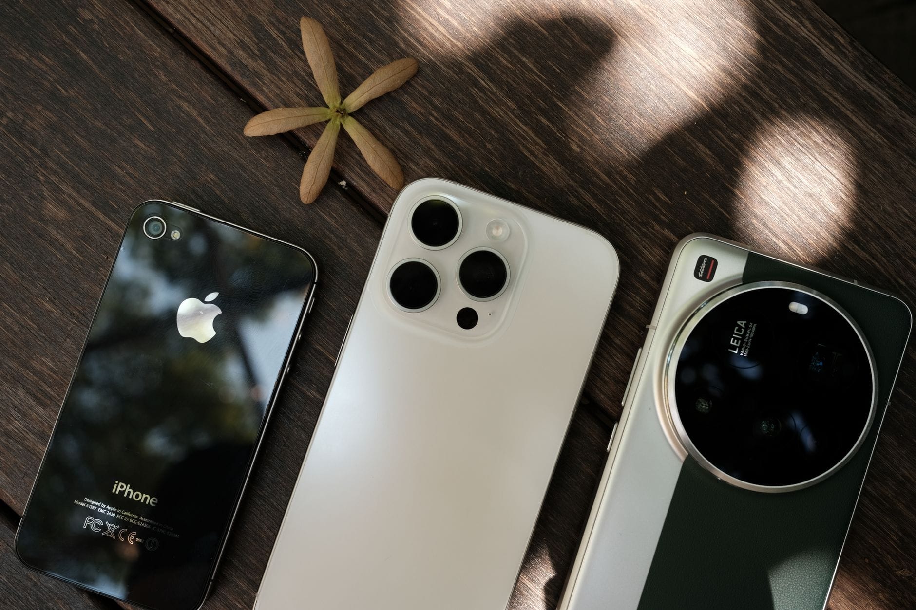 Collection of three modern smartphones displayed on a wooden table surface. — new siri release date iphone 2026