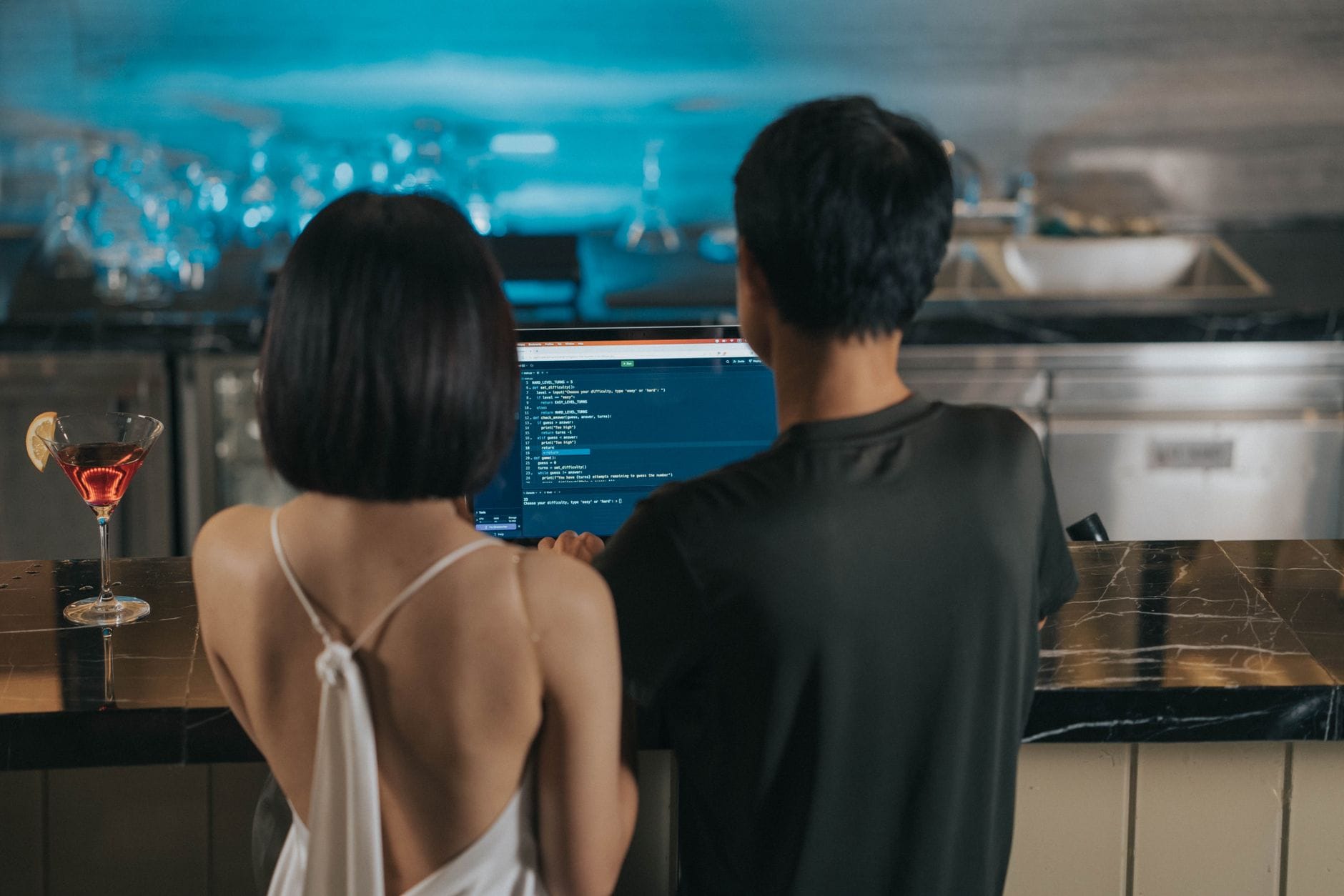 Couple coding together at a bar counter, drinks nearby, casual atmosphere. — github copilot review 2026